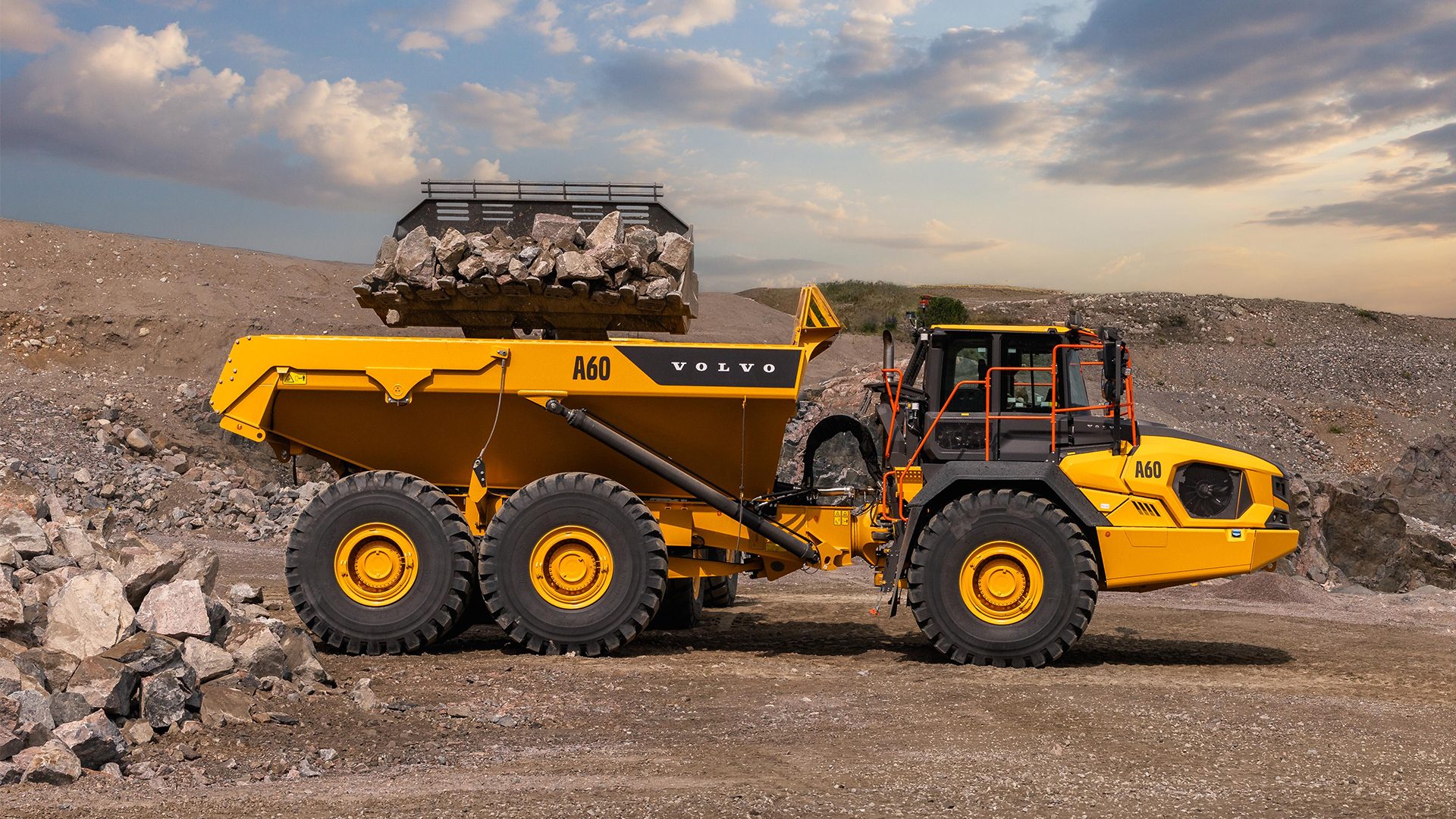 A yellow Volvo A60 articulated dump truck, loaded with rocks, in a quarry under a cloudy sky.