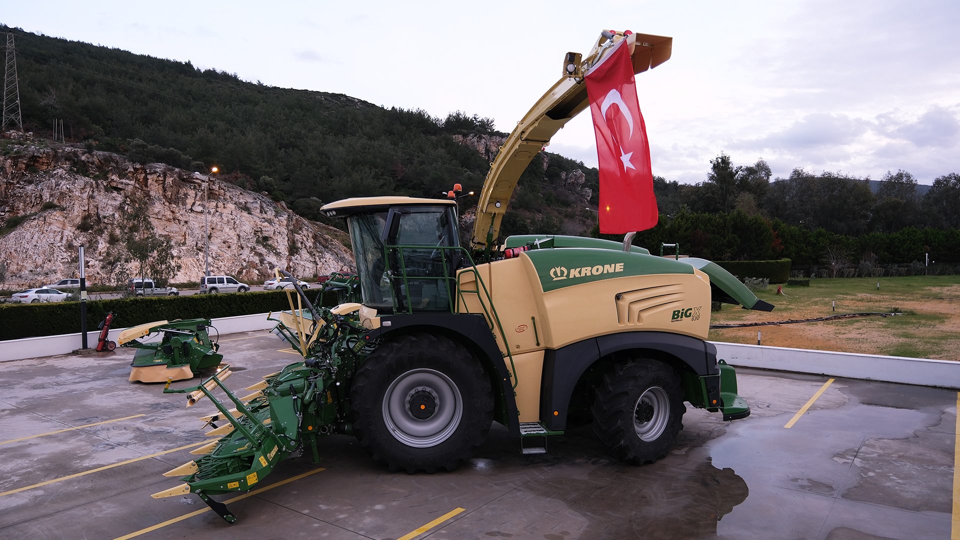 Krone Big X forage harvester with Turkish flag parked outdoors, rocky hill in background.