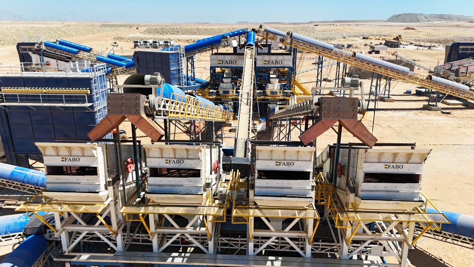 Aerial view of a large FABO crushing and screening plant with multiple conveyors in a desert landscape.