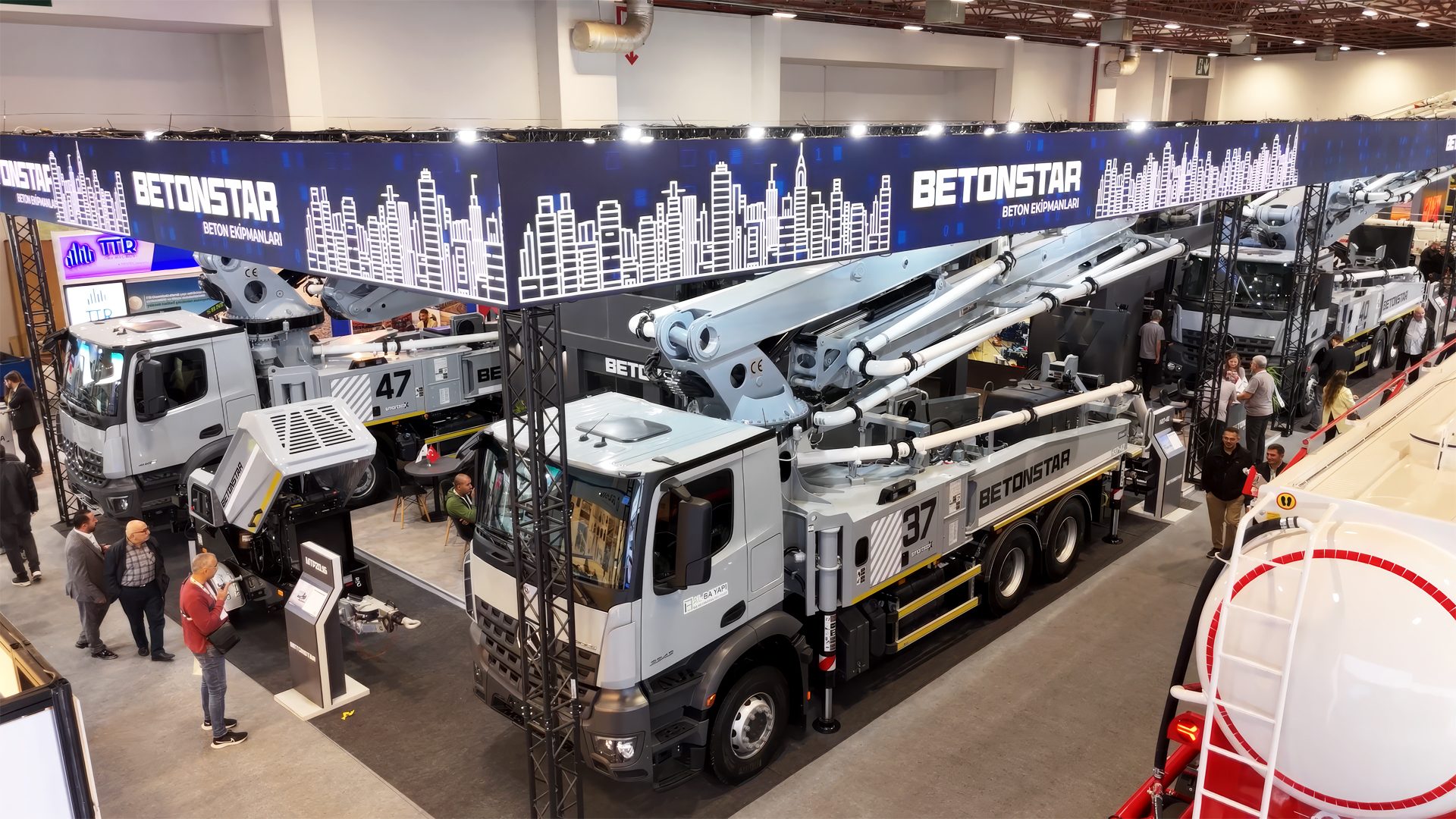 BETONSTAR concrete pump trucks with large booms on display at an indoor exhibition.