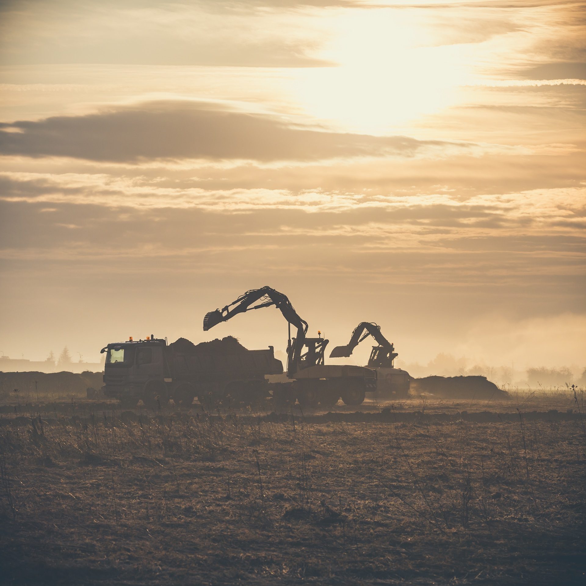 Silhouettes of excavators and a dump truck on a construction site at golden hour.
