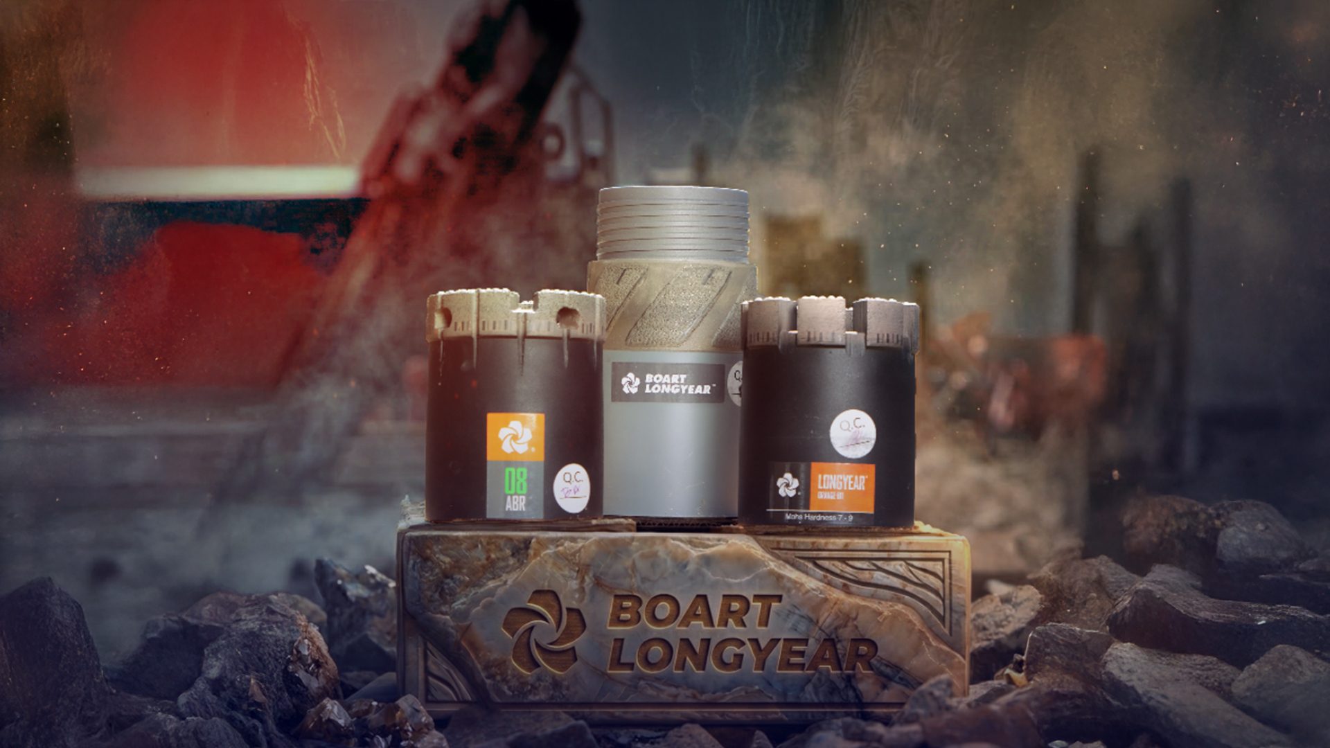 Three Boart Longyear core drill bits on a branded stand, surrounded by rocks and dust.