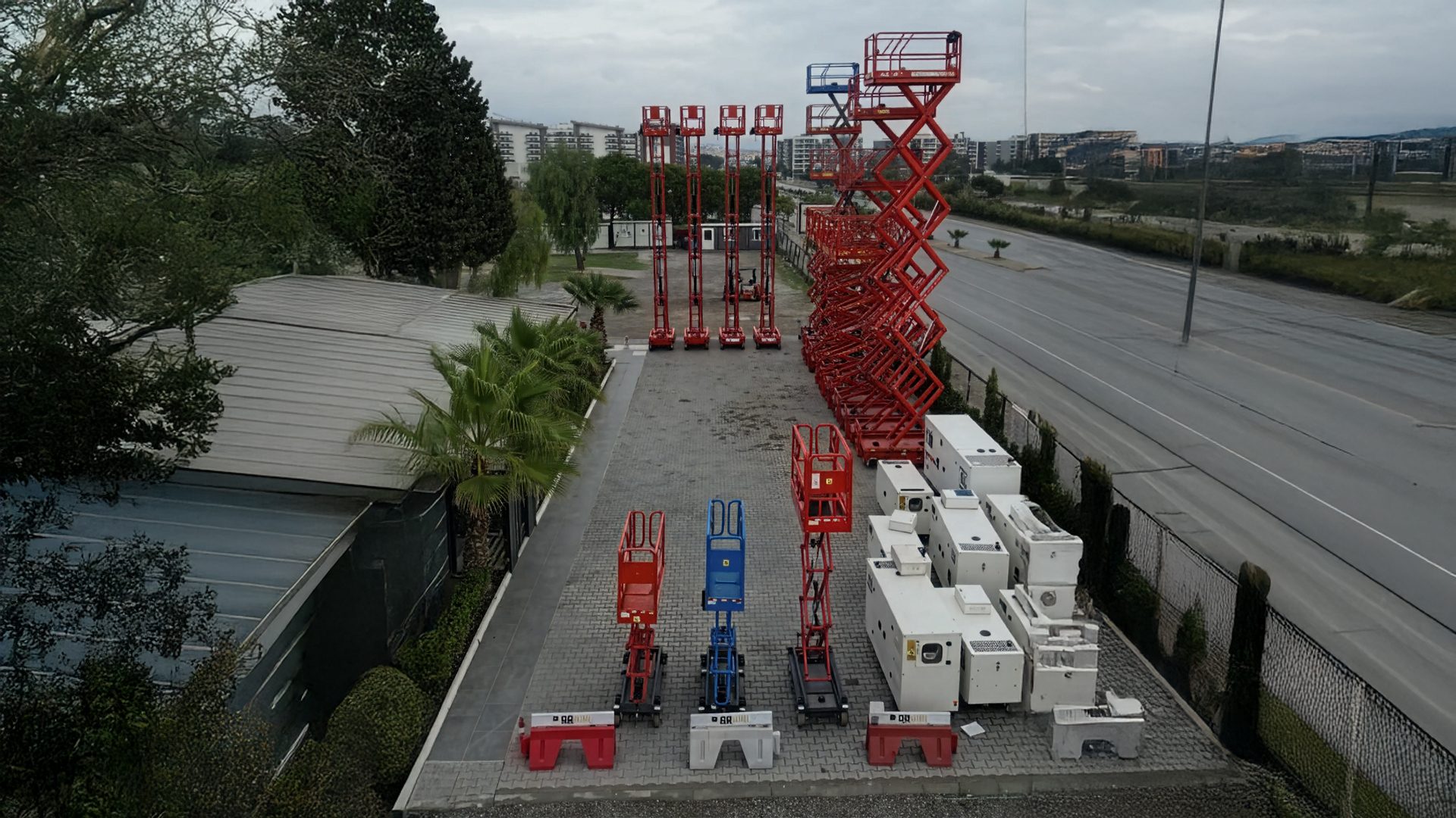 Industrial equipment lot with red scissor lifts and white machinery next to a road.