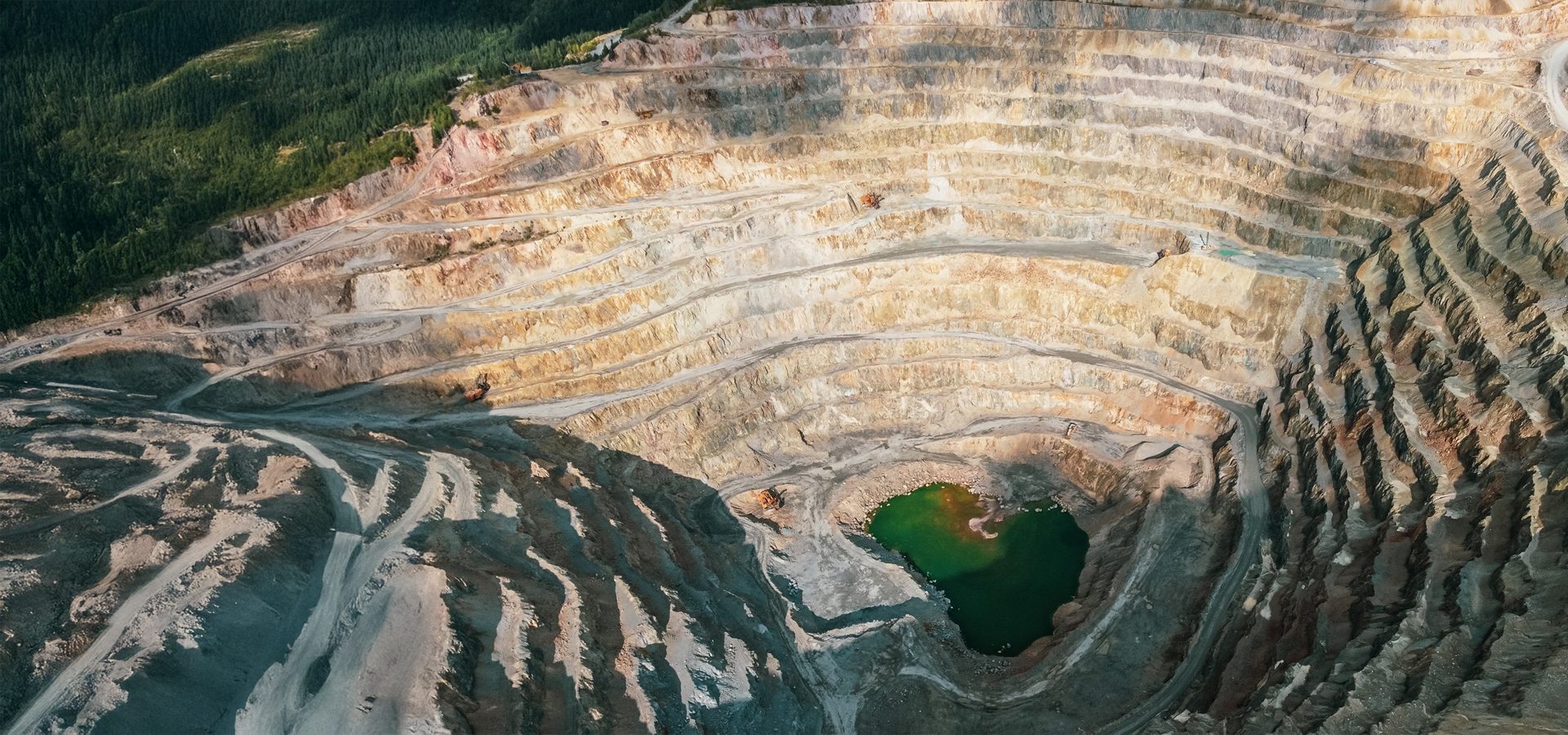 Aerial view of a vast terraced open-pit mine with a vibrant green lake at its deep center.