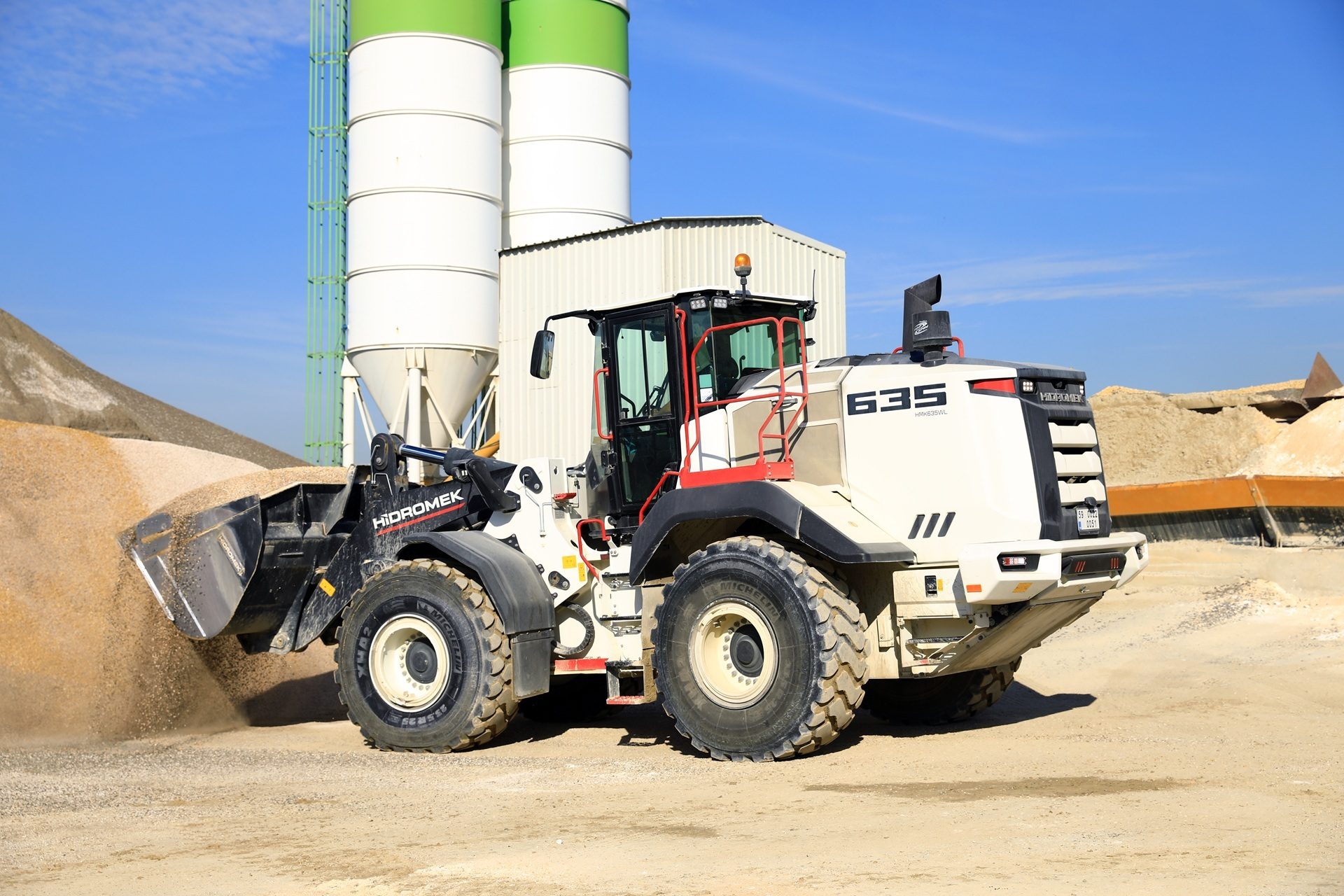 White wheel loader scoops sand at an industrial site.