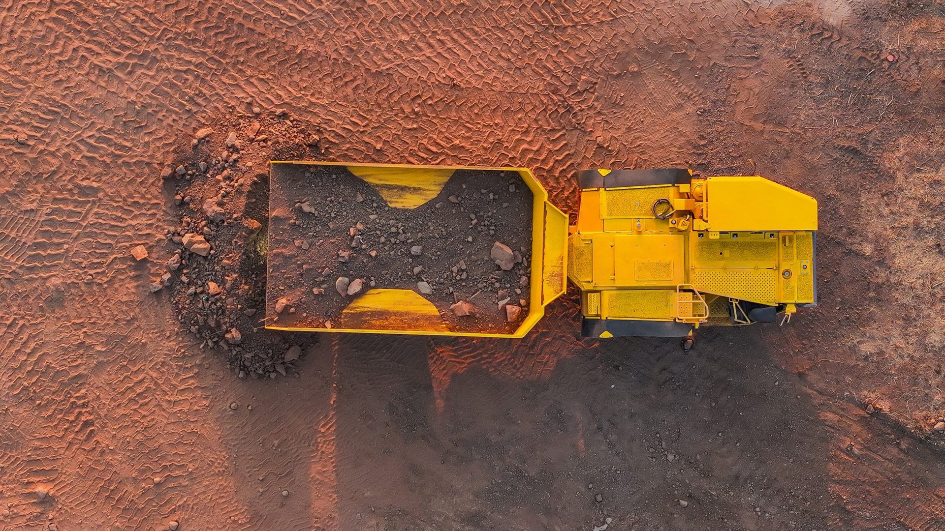 Aerial view of a yellow mining truck dumping rocks on red earth.