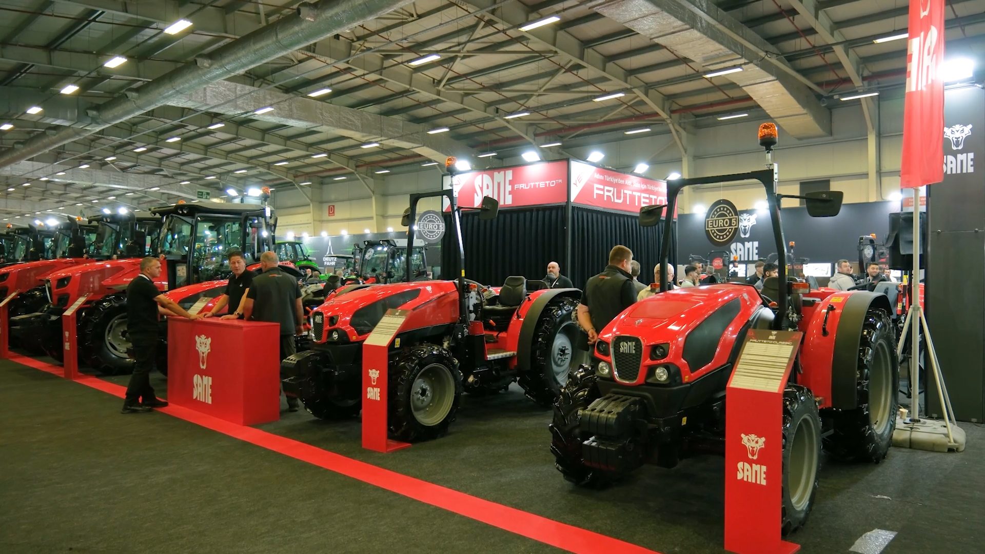Red SAME tractors on display at an indoor exhibition with people.