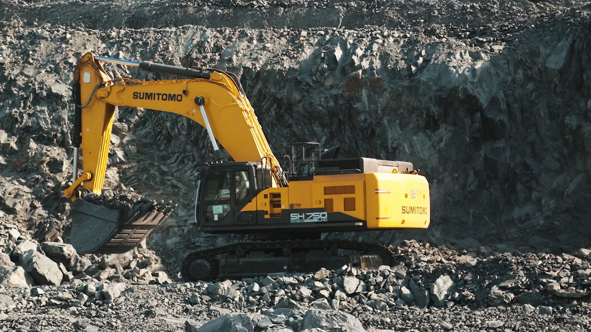 Yellow Sumitomo SH750 LHD excavator working in a rocky quarry.