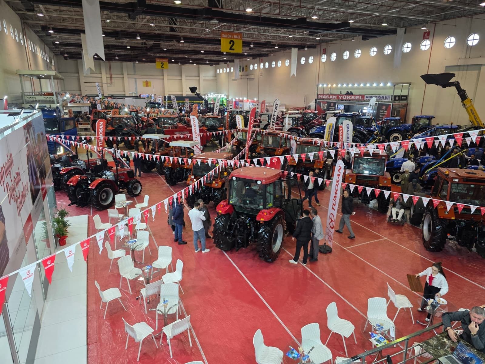 Indoor tractor trade show with numerous red and blue tractors, attendees, and brand banners.