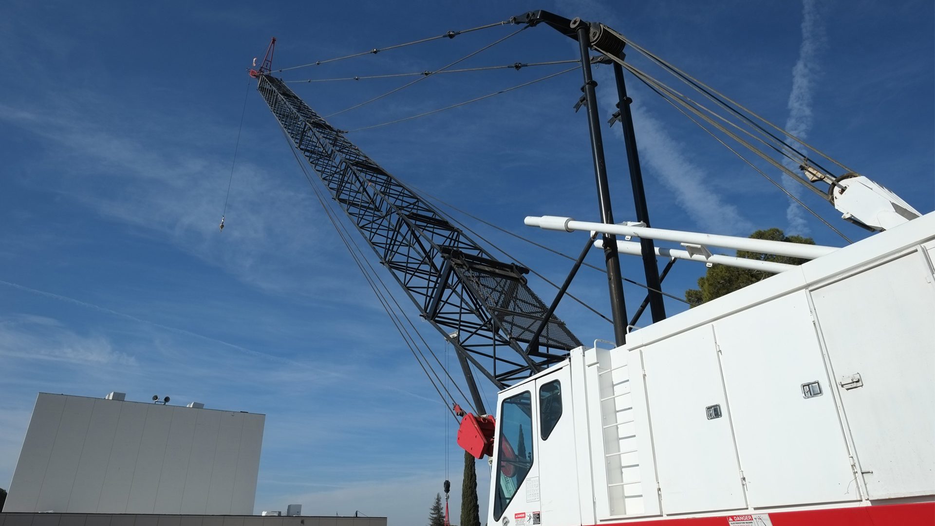 White and black lattice boom crane reaching into a clear blue sky.