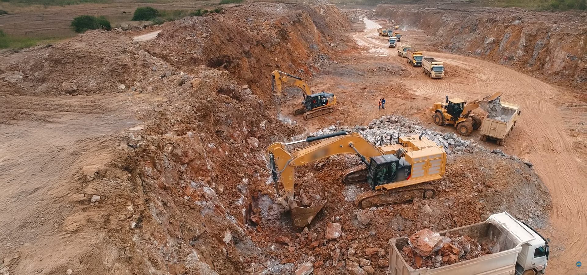 Heavy excavators and dump trucks actively working in a large open-pit mine.