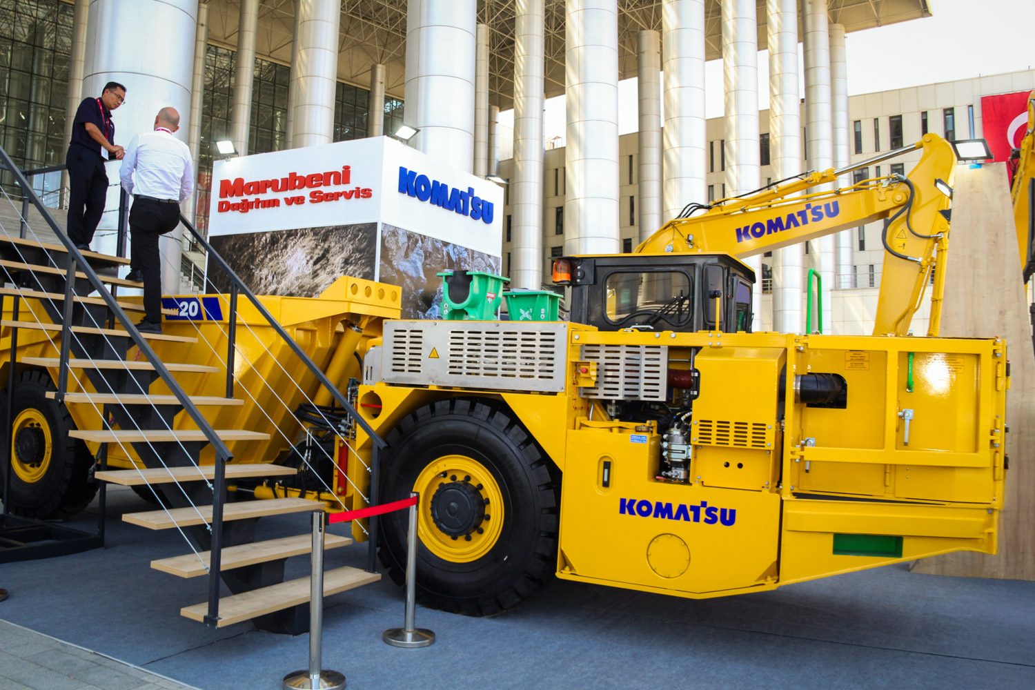 Yellow Komatsu heavy machinery, men on stairs, "Marubeni" and "Komatsu" signs.