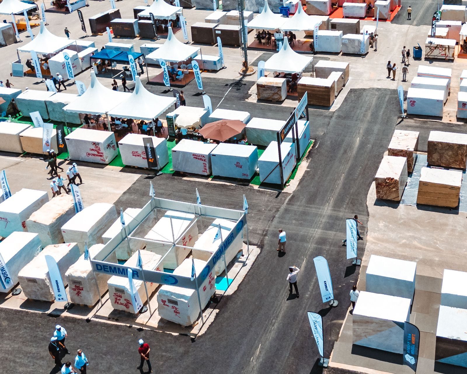 Aerial shot of an outdoor stone block trade fair with tents, banners, and people.