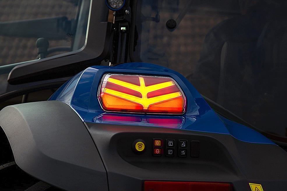 Close-up of a blue tractor's rear taillight with illuminated red and yellow patterns and control buttons.