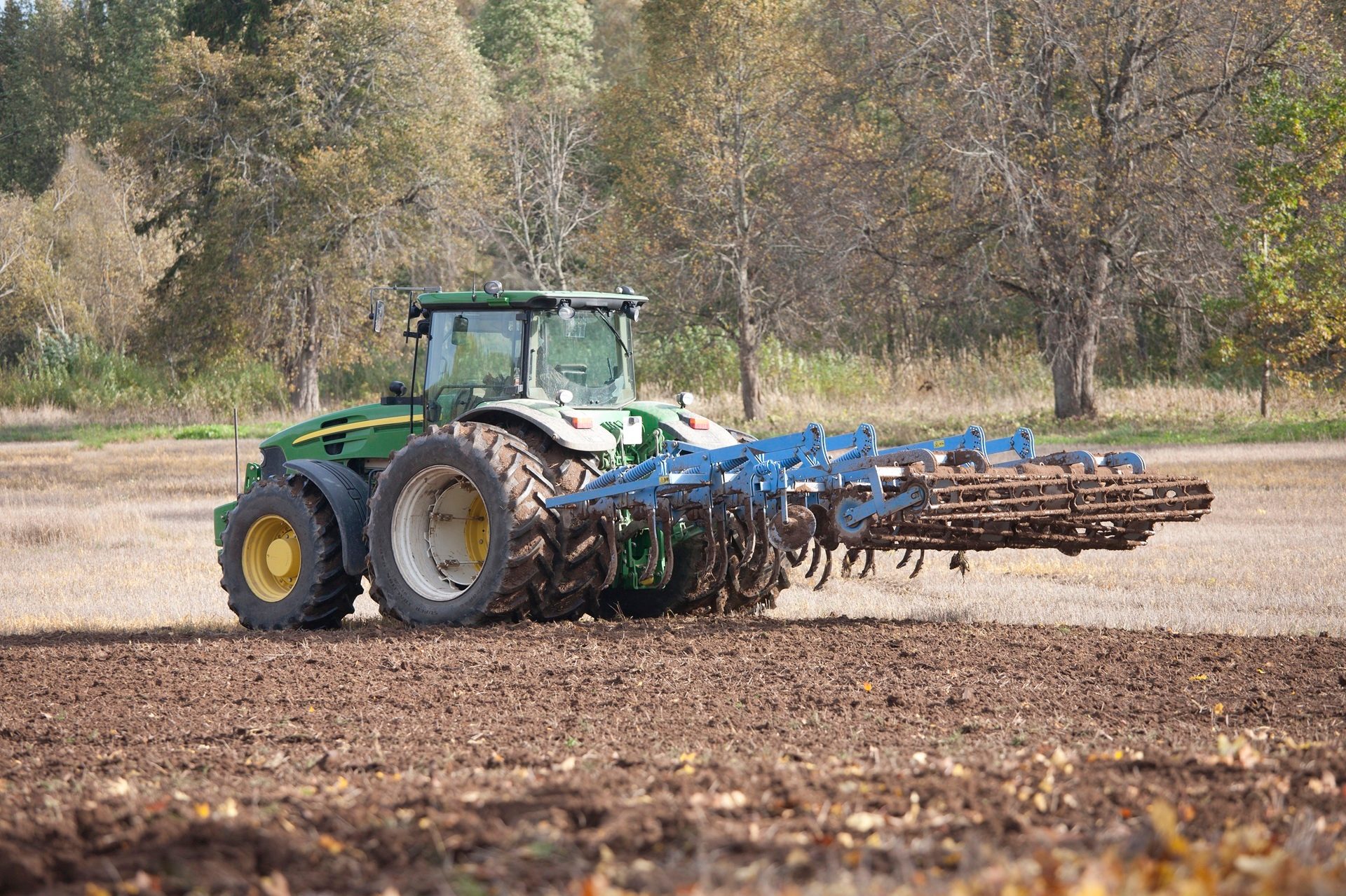 Green tractor with blue tillage implement working in a fall field.