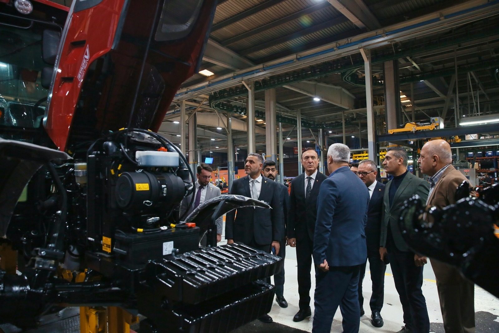 Group of men inspecting a red tractor with its engine exposed inside a factory.