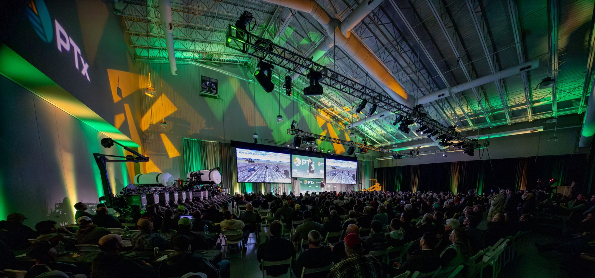 Conference with an audience, screens showing PTx, farming content, and agricultural machinery.