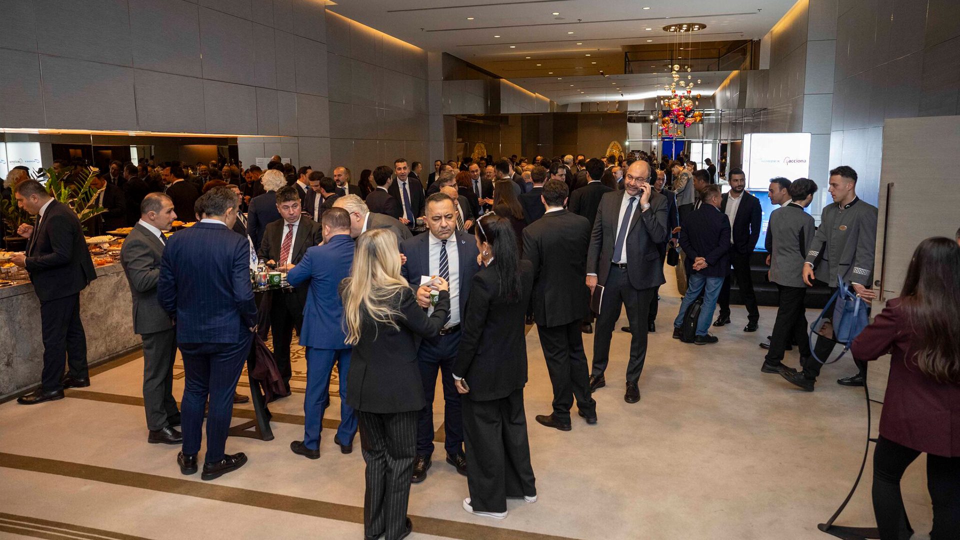 Many business professionals in suits gathered at a busy networking event with food stations.