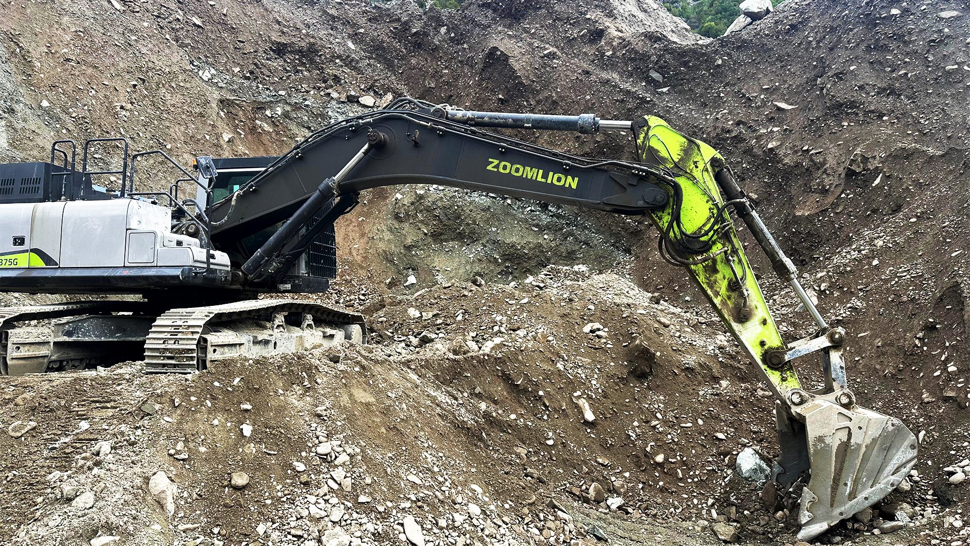 Zoomlion excavator with a neon green arm digging in a rocky, dirt-filled construction site.