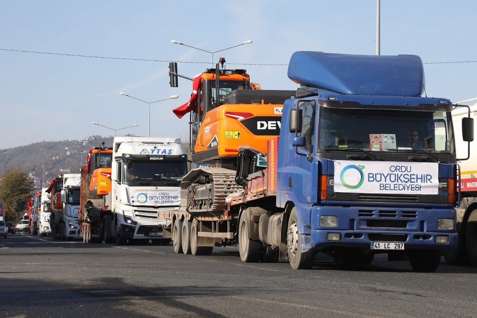 Convoy of Ordu Municipality trucks carrying excavators, adorned with Turkish flags.