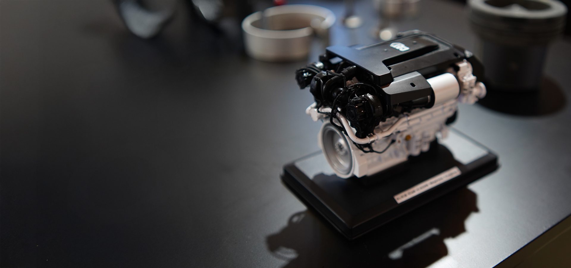 A black and white miniature engine model sits on a dark, reflective surface.