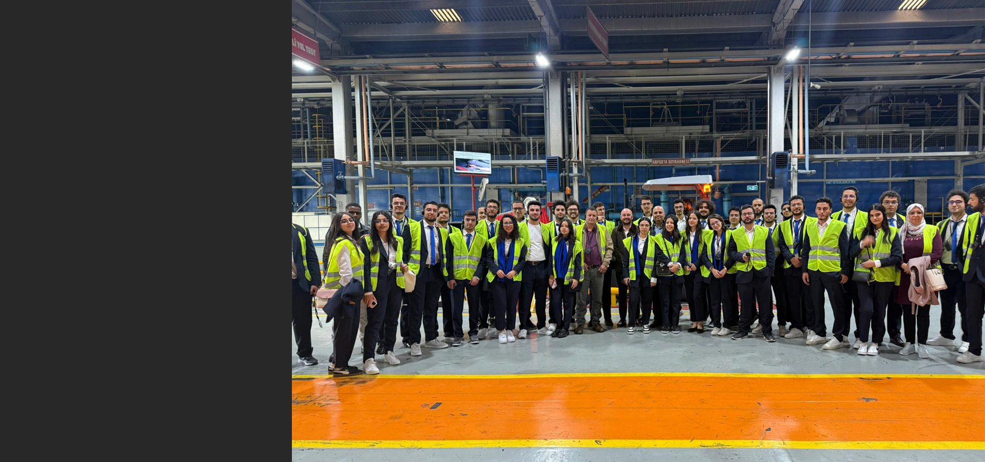 Group of young people in suits and safety vests standing in a factory.