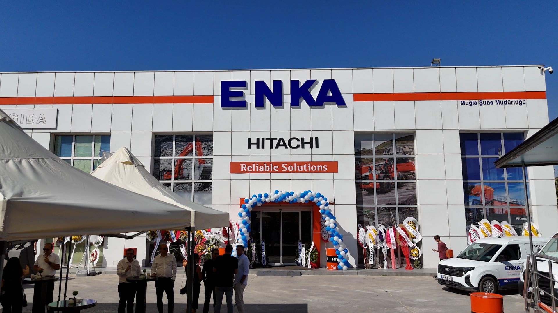 ENKA-HITACHI Muğla Branch building with 'Reliable Solutions' sign and an outdoor event.