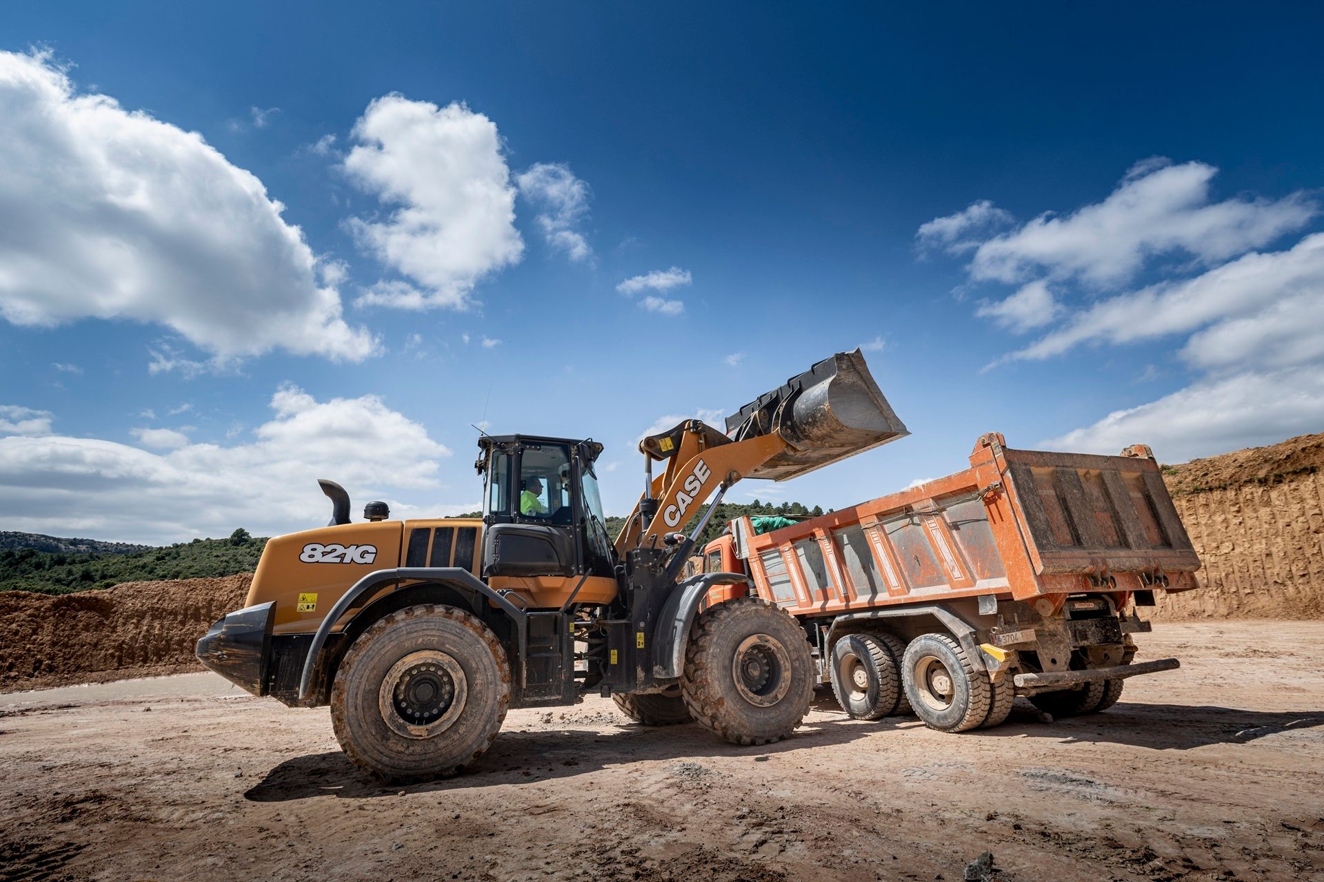 Case loader filling a dump truck on a sunny construction site.
