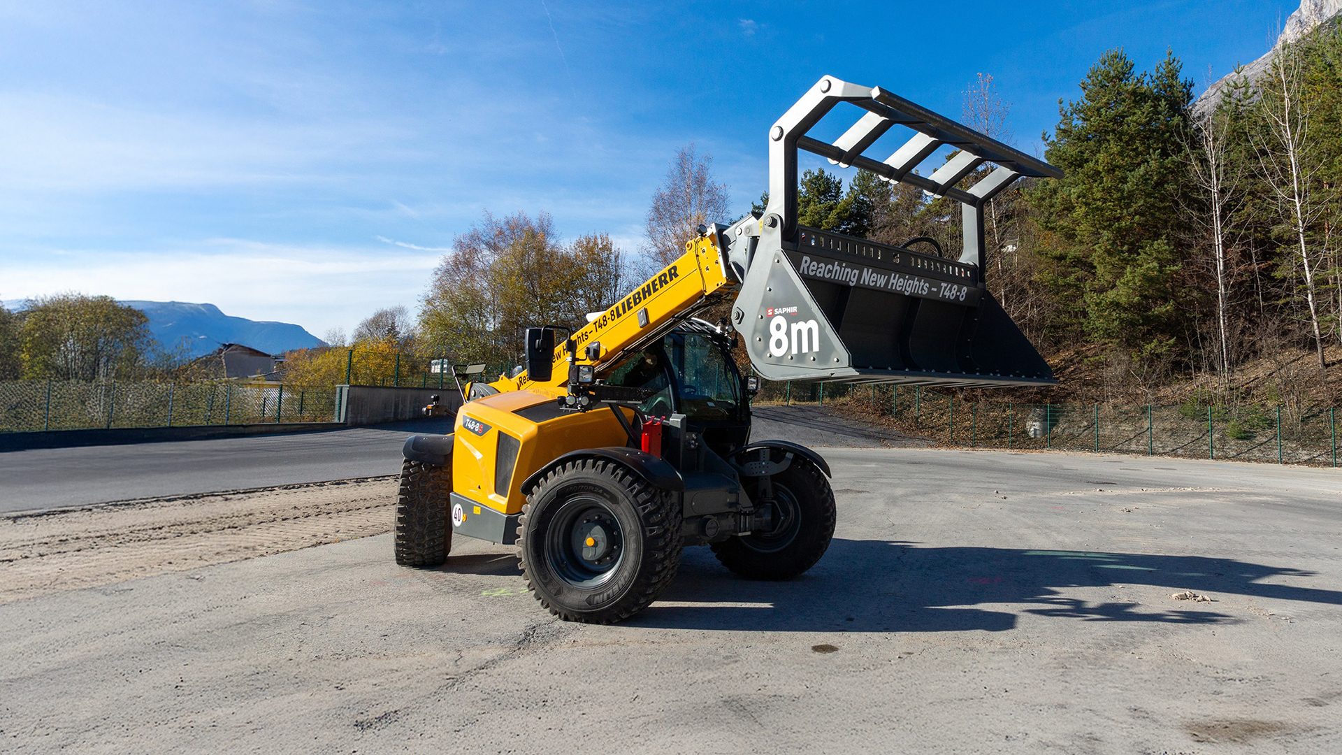 Yellow Liebherr telehandler with a large bucket attachment, featuring "8m" and "Reaching New Heights" text.