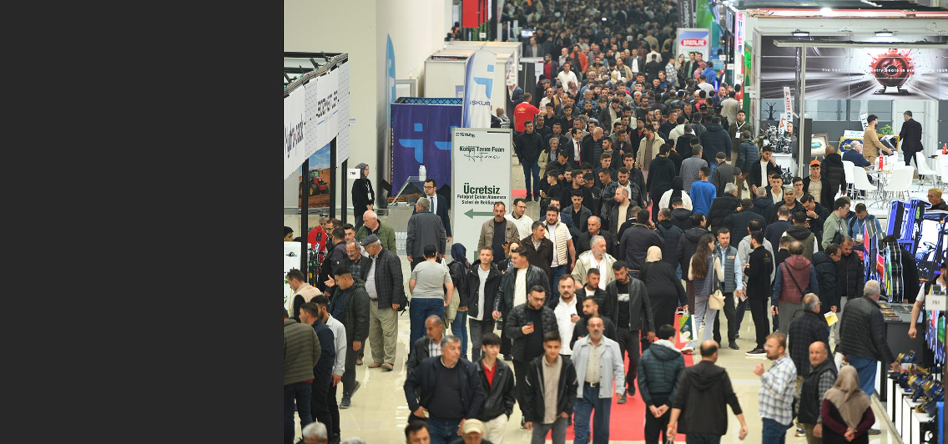 Large crowd of people walking through a bustling exhibition hall with various booths.