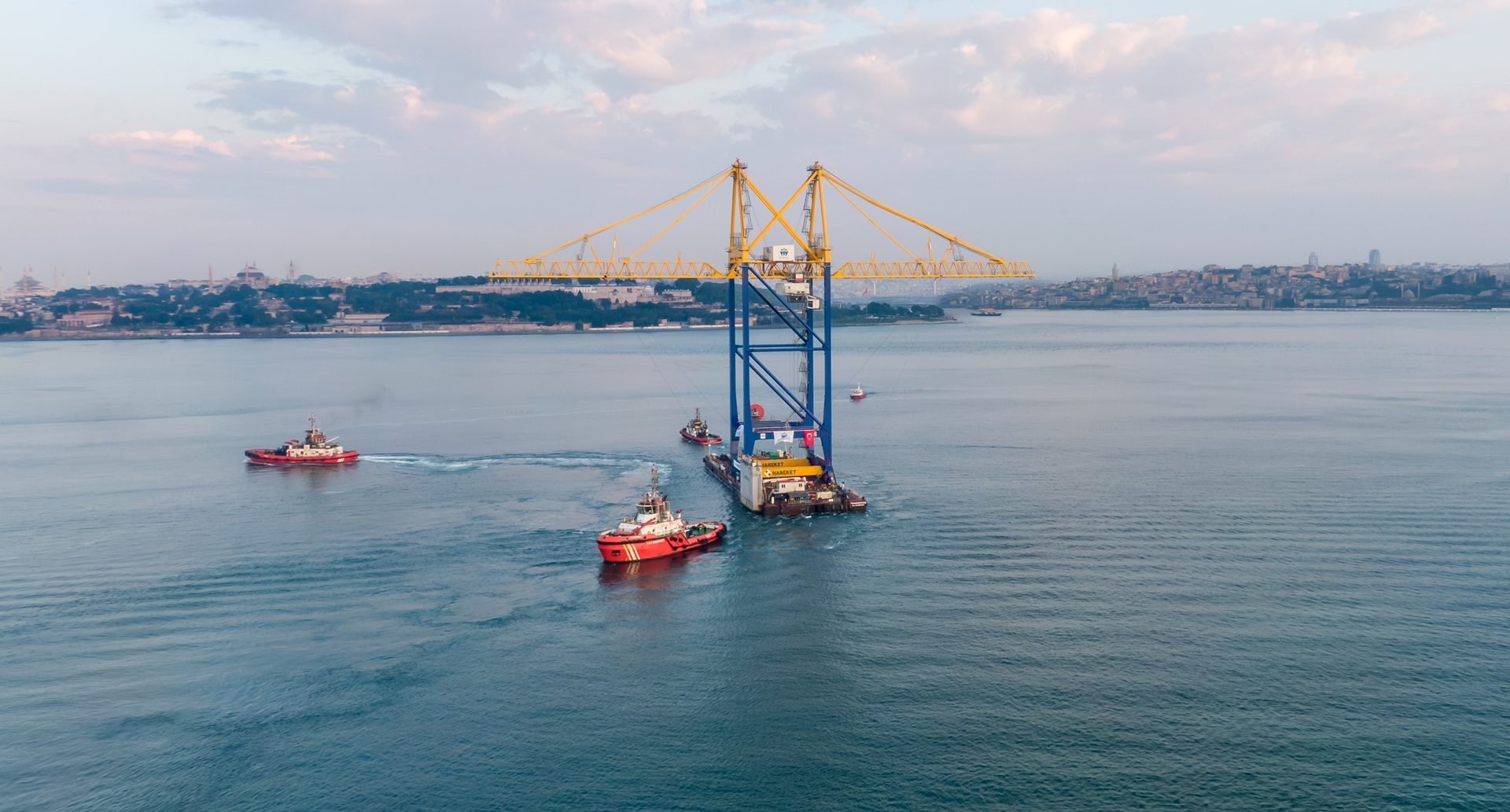 Giant yellow and blue gantry crane on a barge, tugboats, Bosphorus, Istanbul skyline.