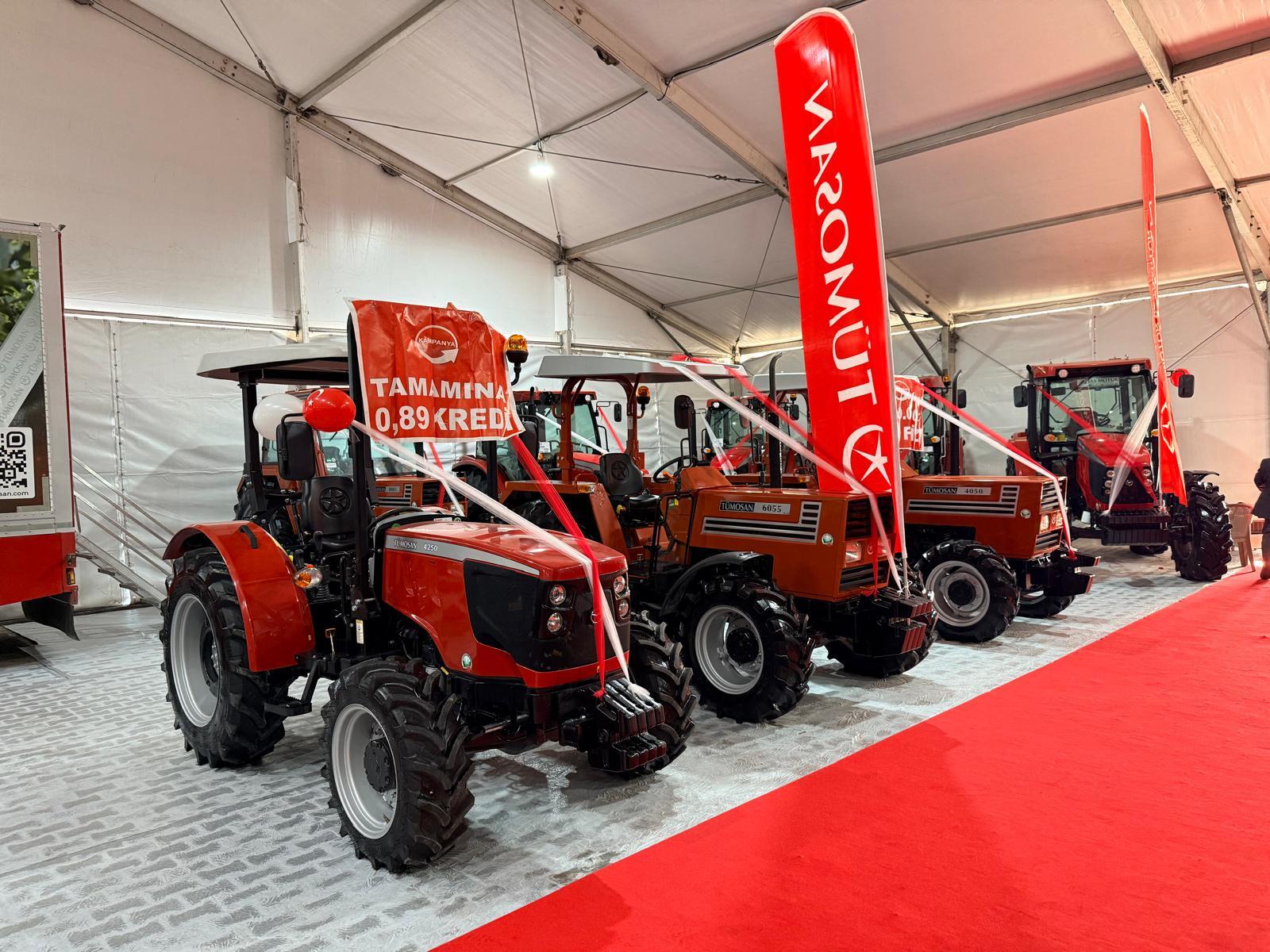 Several red and orange Tümosan tractors displayed under a tent with promotional banners.