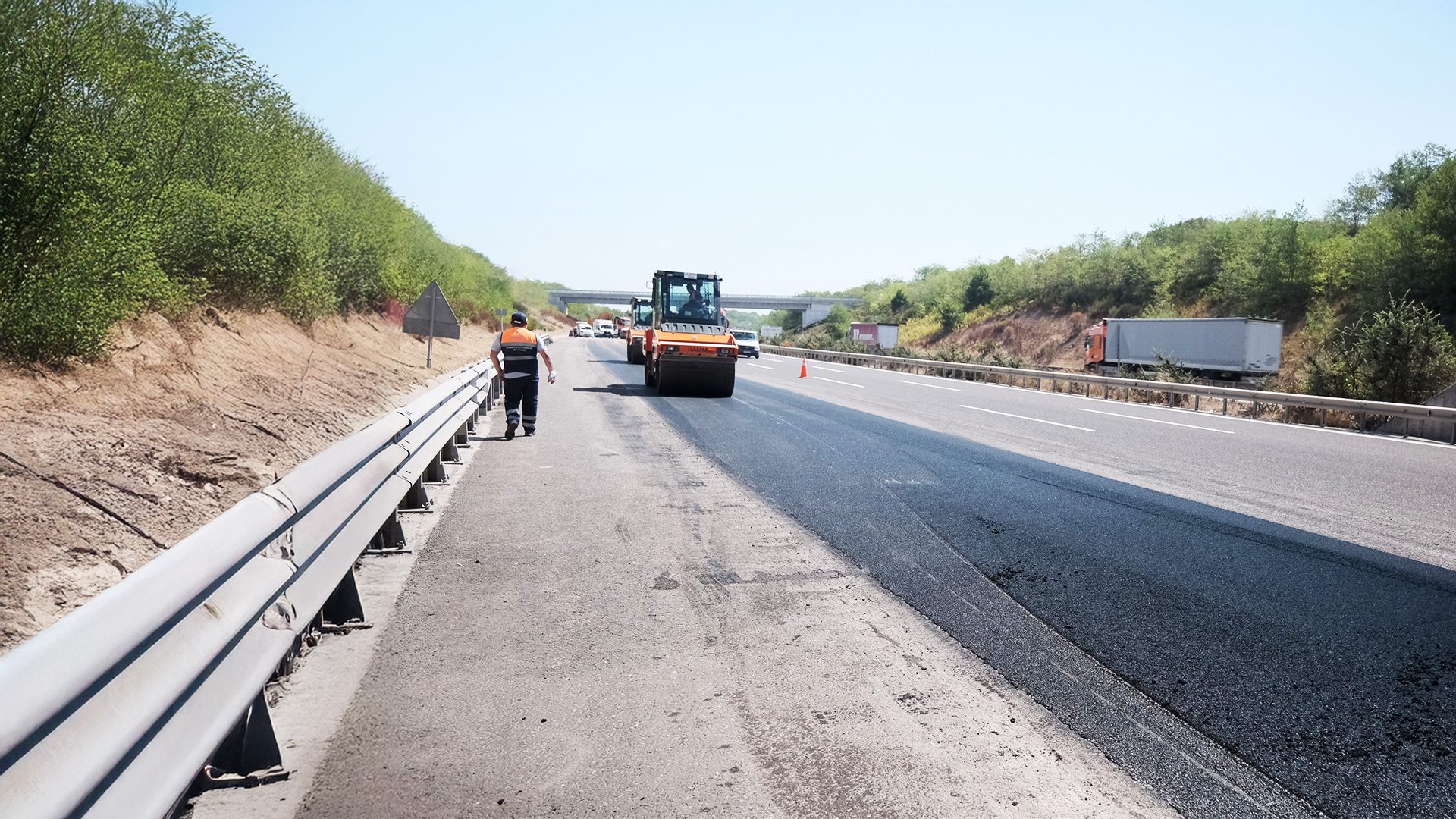 Highway construction: worker and road roller paving fresh asphalt.