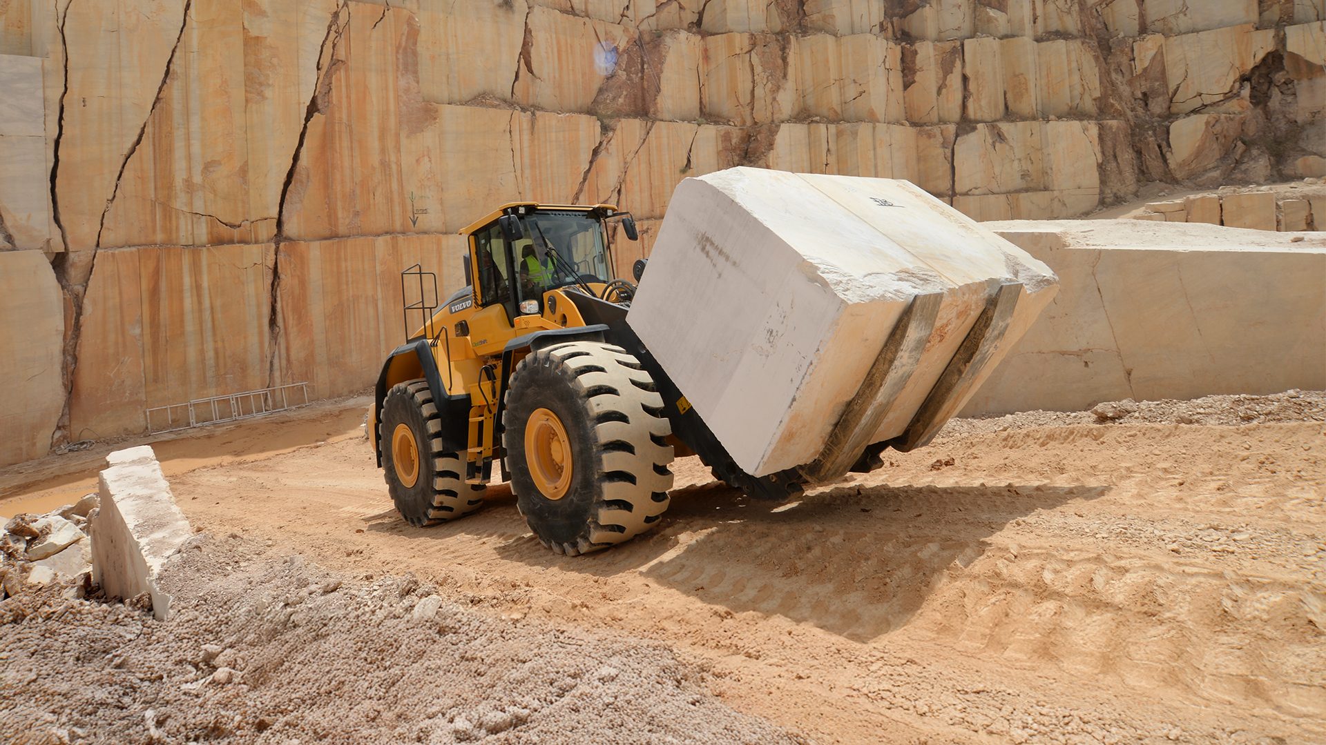 Yellow front-end loader carrying a huge stone block in a quarry.