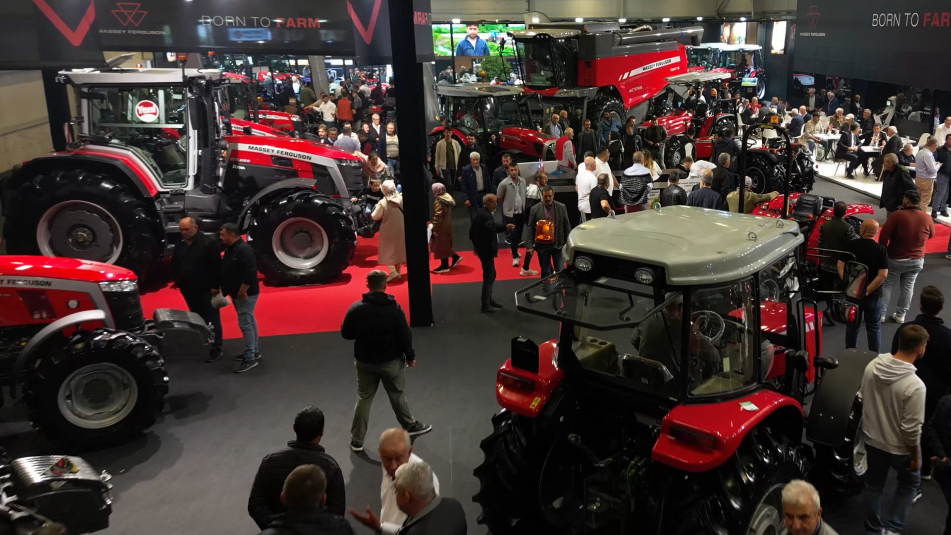 A crowded agricultural exhibition showcasing various red Massey Ferguson tractors and farm machinery.