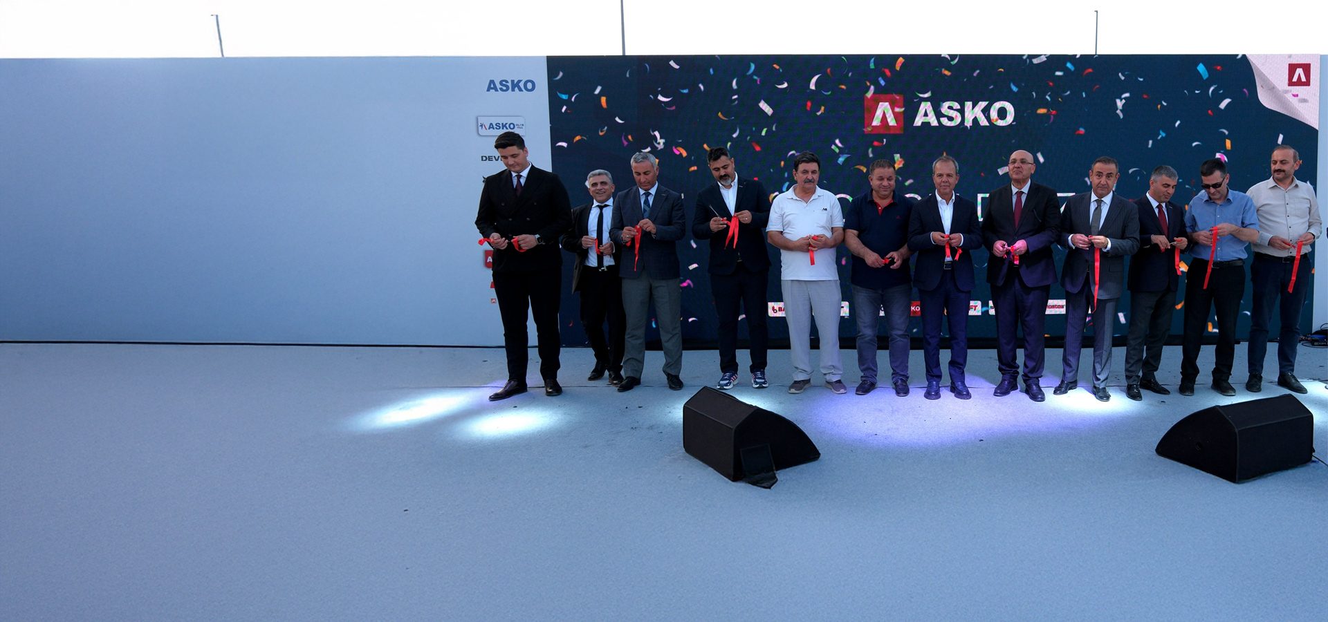 Men holding red ribbons at an ASKO event with confetti background.
