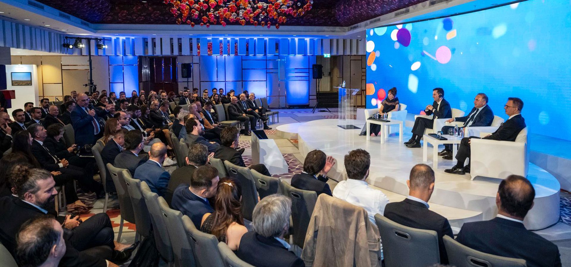 A business conference with a panel on stage and an audience, one attendee asking a question.