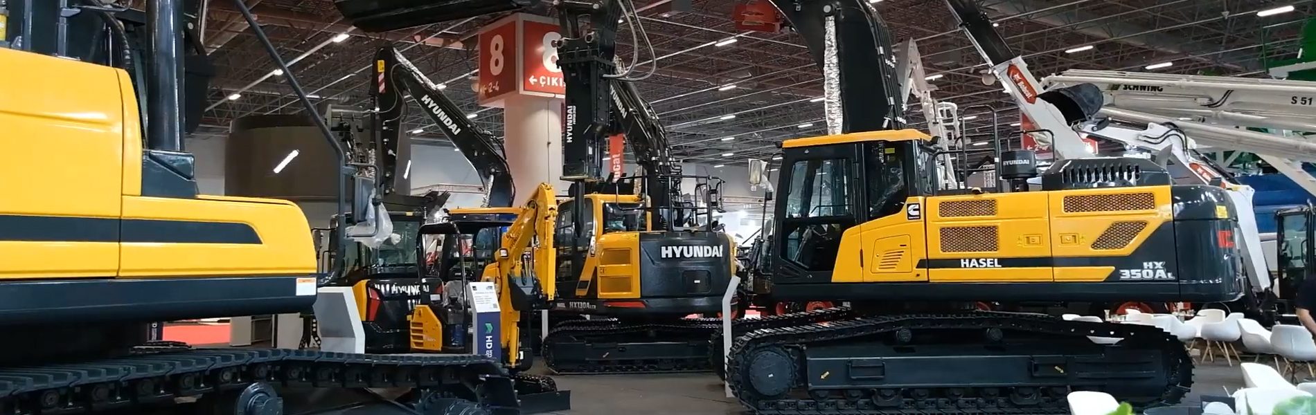 A wide shot of several large yellow and black Hyundai excavators displayed at an indoor exhibition.