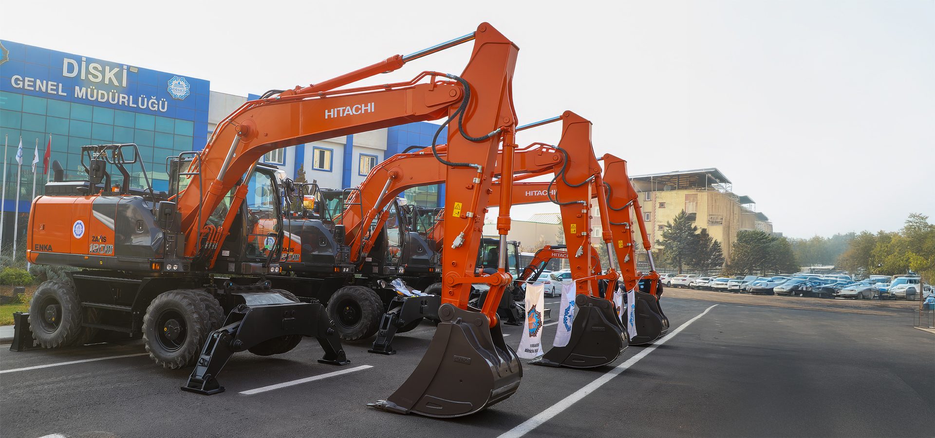 Orange Hitachi excavators lined up in front of a building and a parking lot.