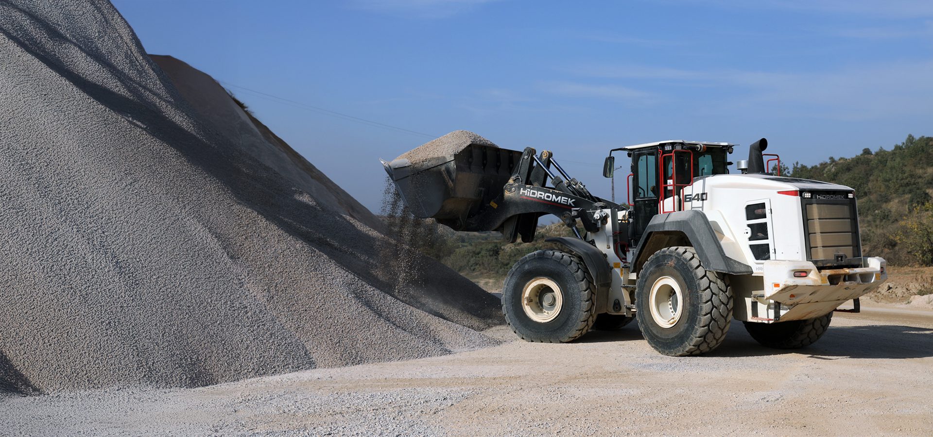 White wheel loader dumping gravel onto a large pile.