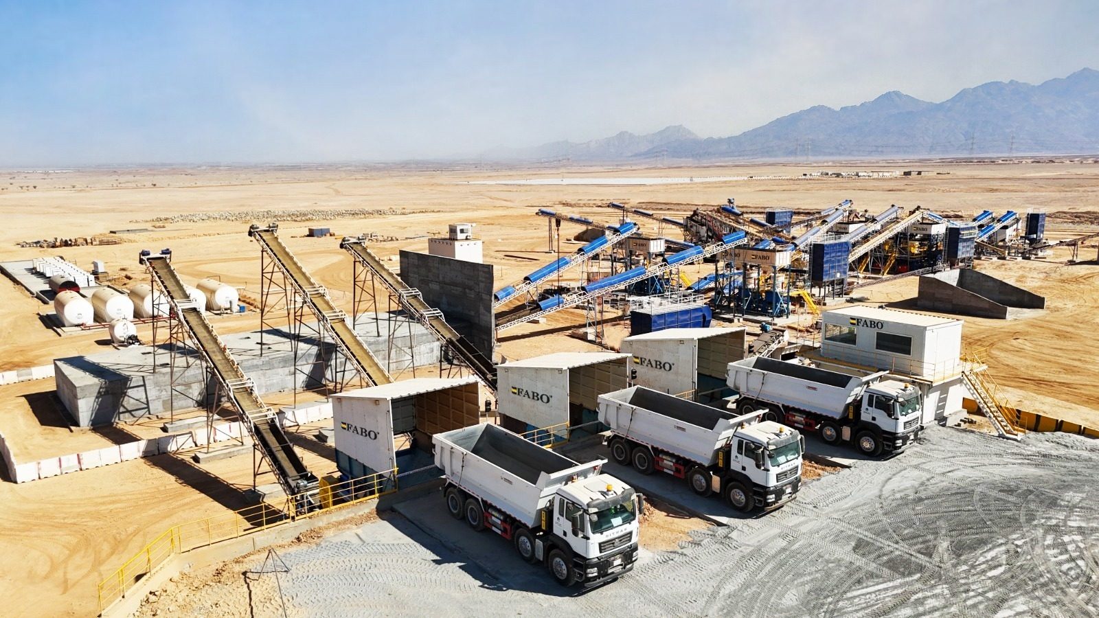 Aerial shot of a FABO industrial quarry in a desert, with conveyor belts, machinery, and dump trucks.