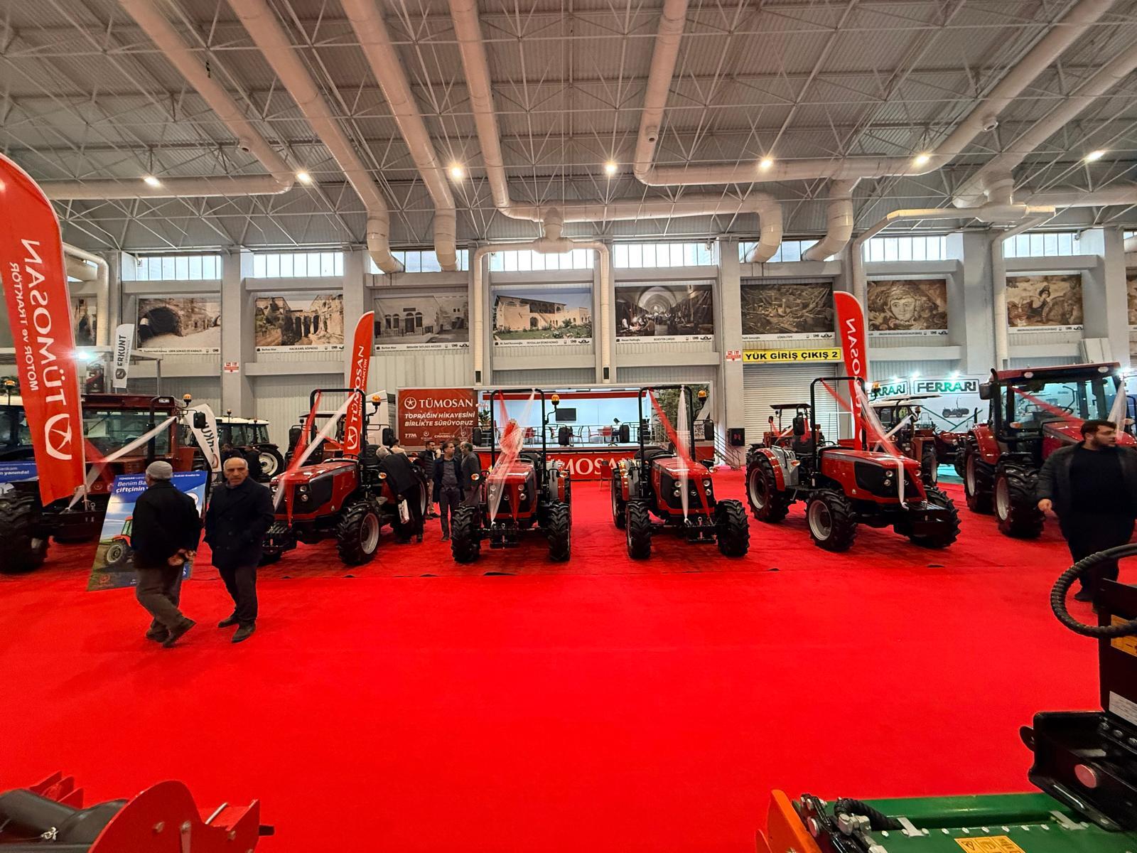 Indoor tractor exhibition: red tractors on red carpet, attendees, and brand banners.