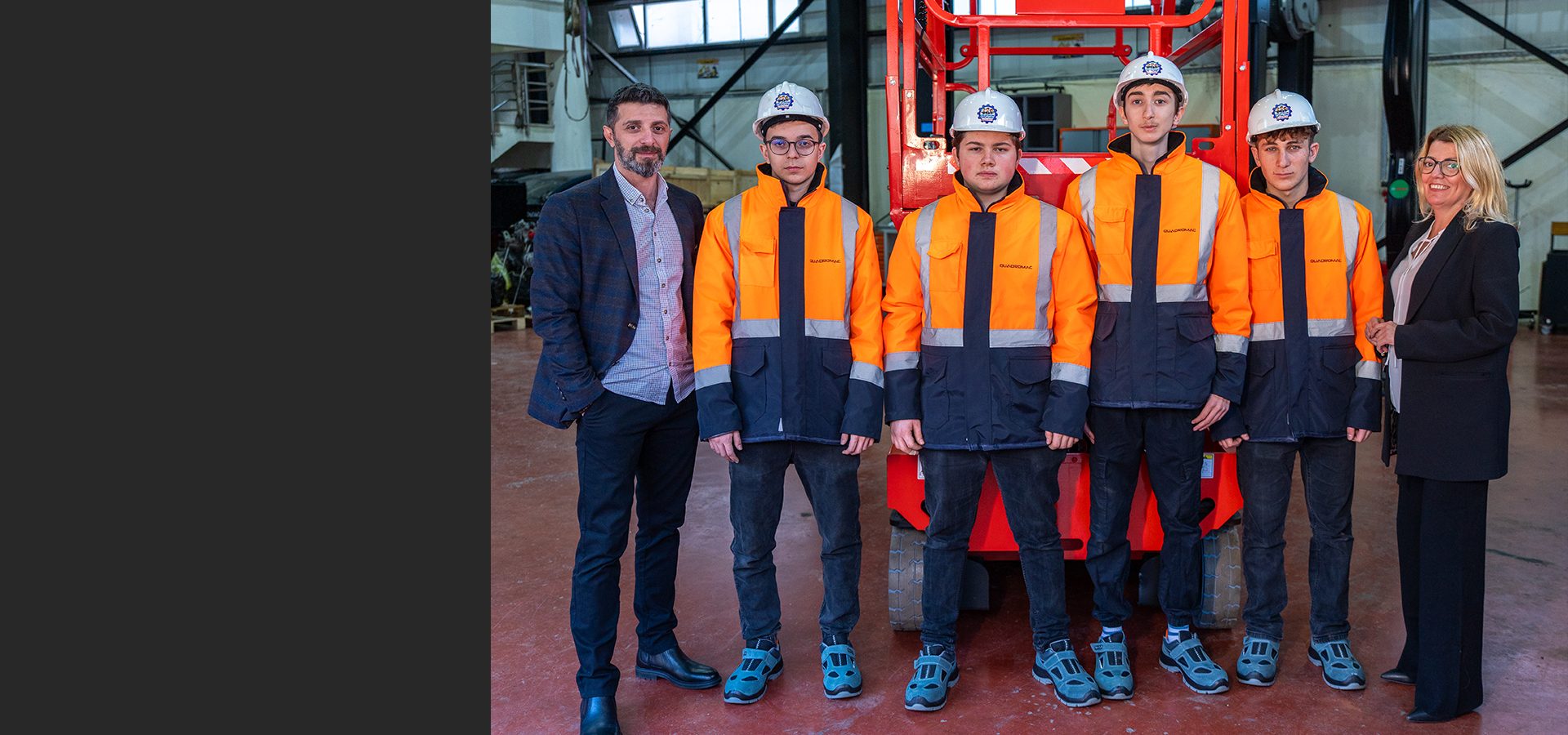 Six people, including four young men in safety jackets and hard hats, posing with two adults.