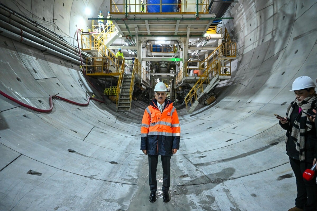 Official in safety gear in concrete tunnel construction, with reporter.