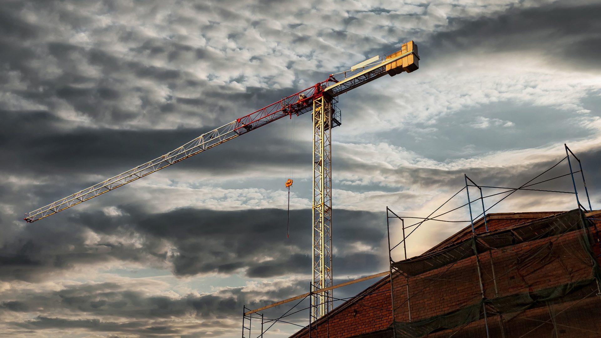 Construction crane and brick building with scaffolding under a dramatic, cloudy sky.