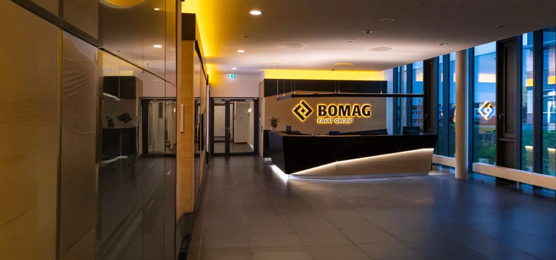 Modern, illuminated office reception with a glowing "BOMAG FAYAT GROUP" logo and a sleek black desk.