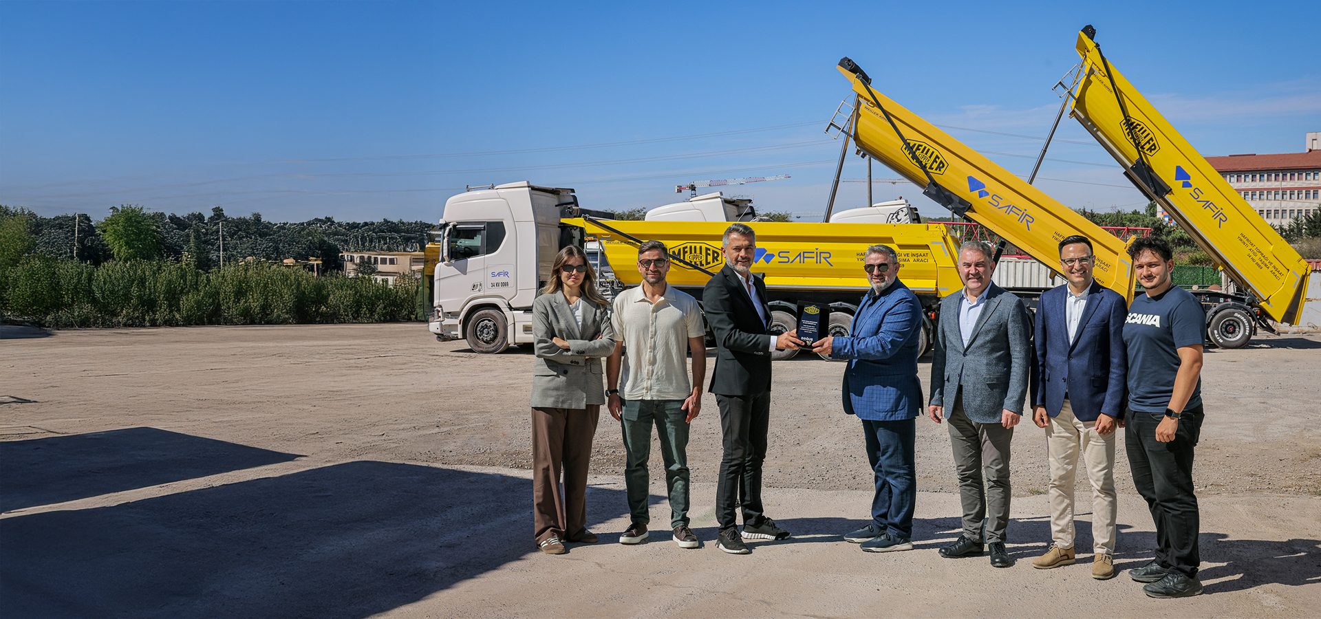 Group of people receiving an award in front of yellow Meiller dump trucks and a white Scania semi-truck.