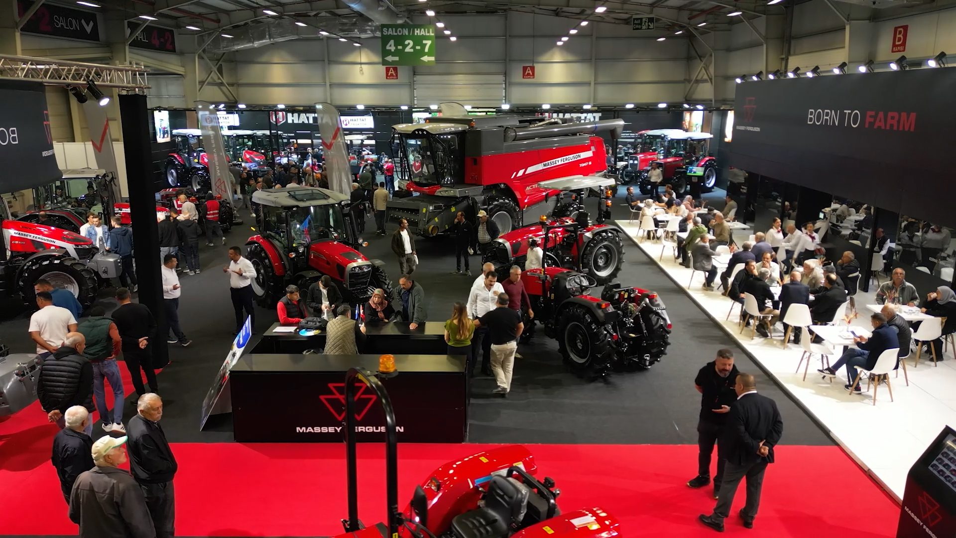 Indoor expo with red Massey Ferguson farm machinery (tractors, combine harvester) and visitors.