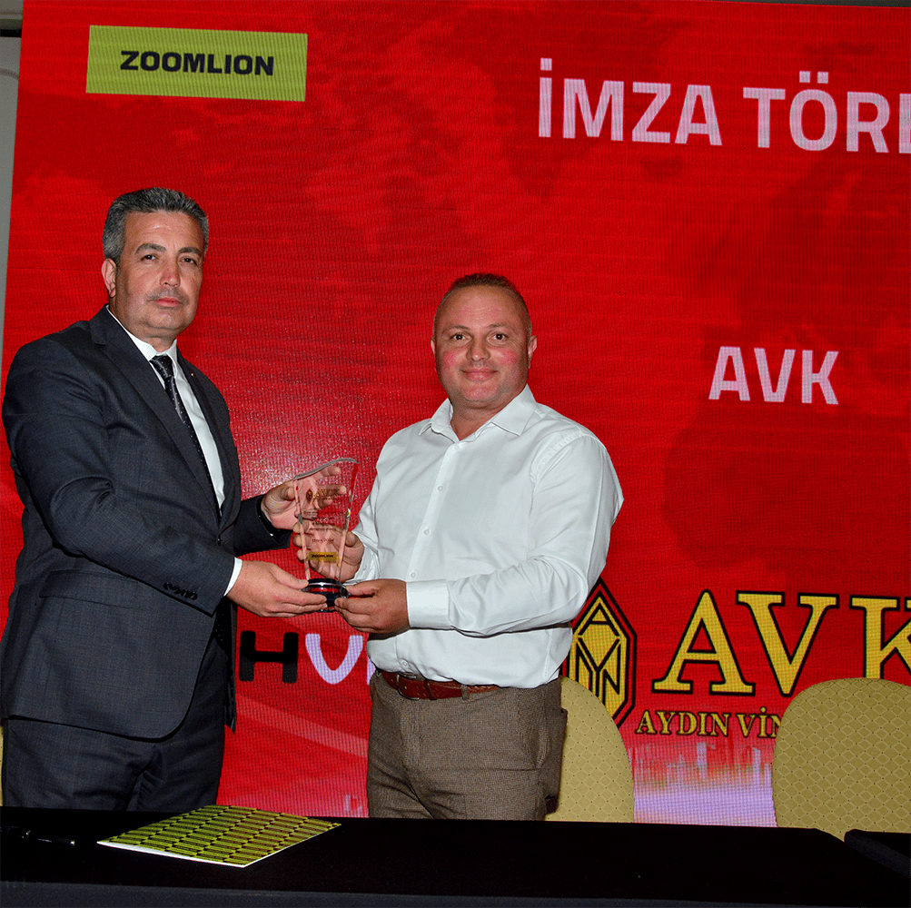 Man in suit presents award to man in white shirt against red background.