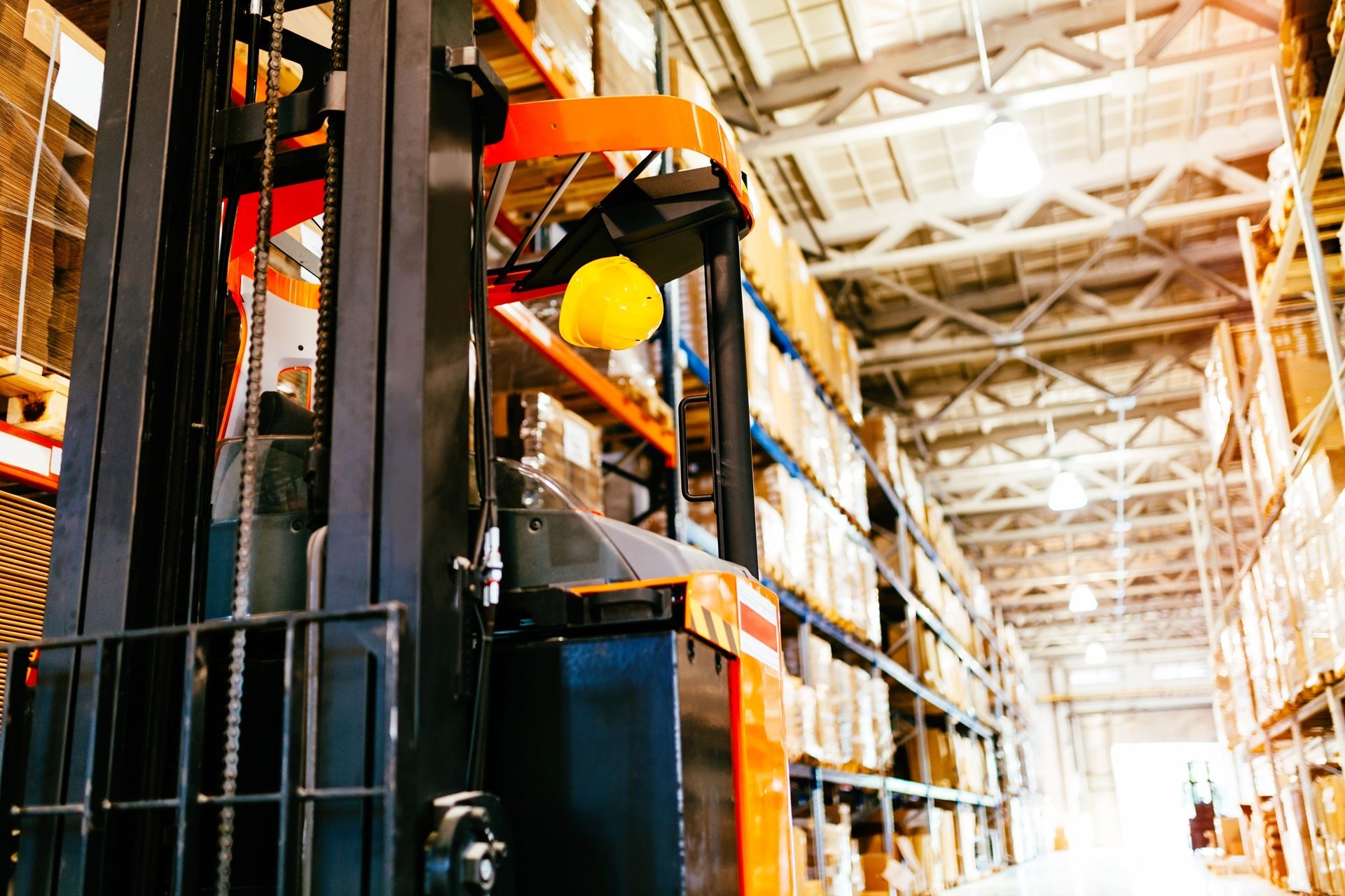 Yellow hard hat hanging on a forklift in a warehouse.